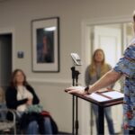 A patient sharing his story in front of an audience at a podium in an office setting with inspirational pictures on the walls