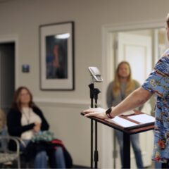 A patient sharing his story in front of an audience at a podium in an office setting with inspirational pictures on the walls