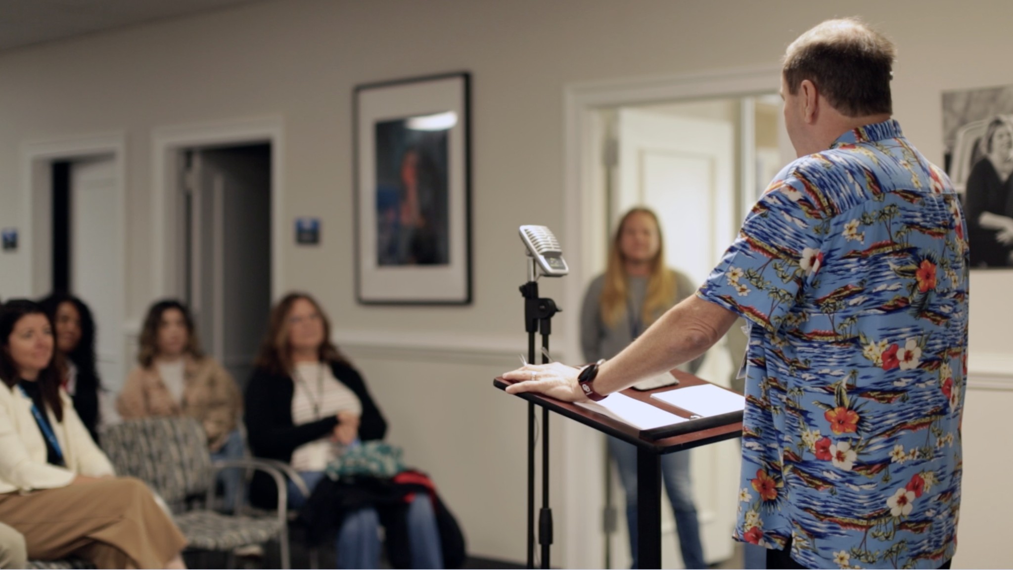 A patient sharing his story in front of an audience at a podium in an office setting with inspirational pictures on the walls